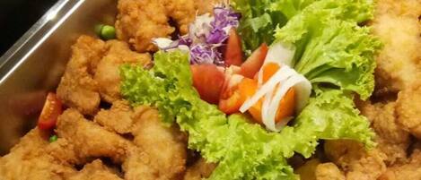 Una bandeja de buffet con trozos de pollo frito, lechuga, tomates y guisantes.