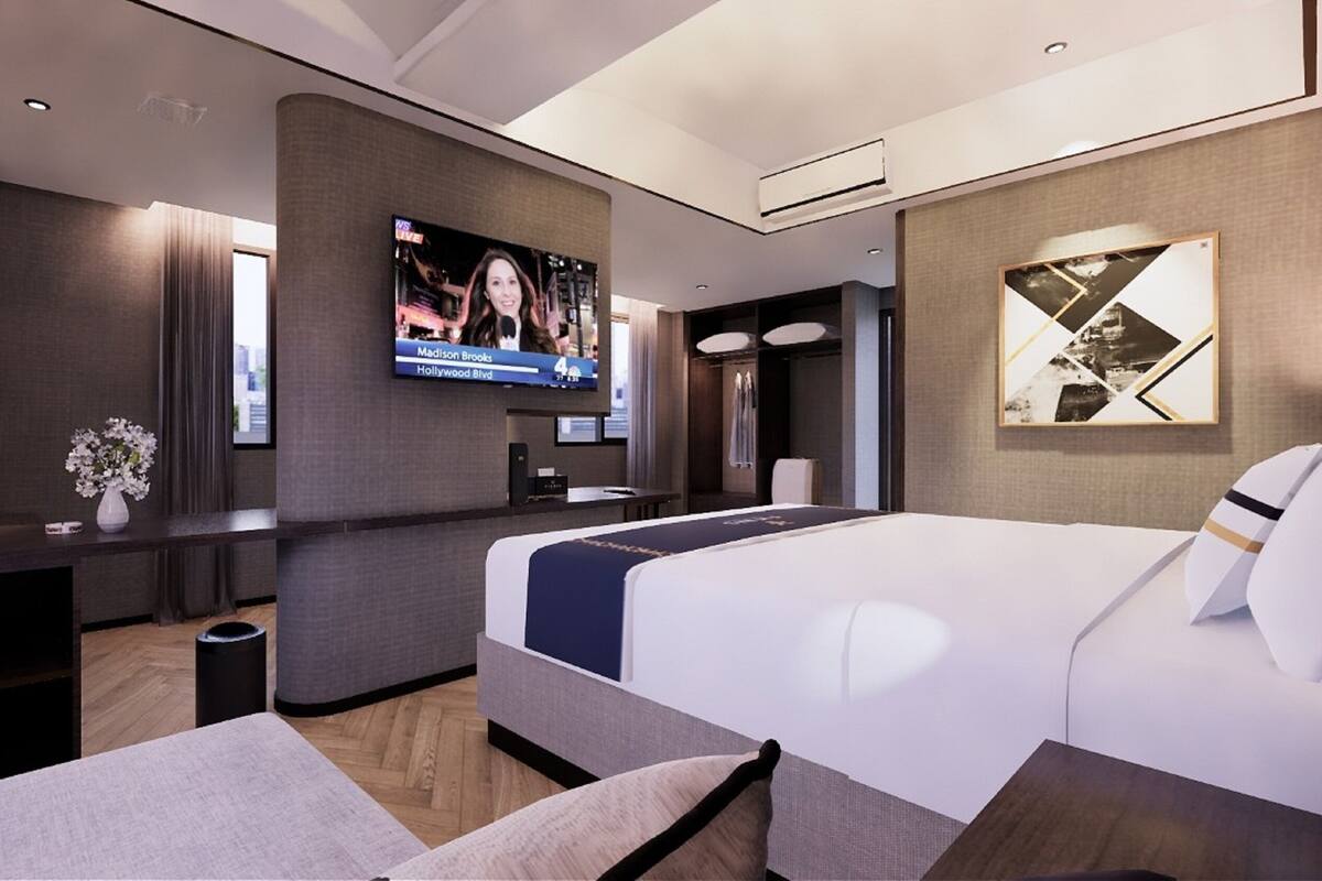 Een moderne hotelkamer met een groot bed, een flatscreen televisie aan de muur, een nachtkastje, een bureau met een stoel en een boekenplank.