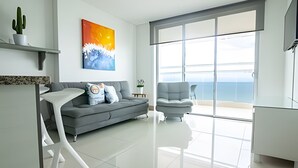 Ein modernes Wohnzimmer mit einem grauen Sofa, einem weißen Couchtisch und einem großen Fenster mit Meerblick.