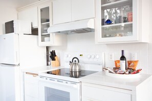 Une cuisine moderne avec des meubles blancs, une bouilloire en acier inoxydable et une variété de collations et de boissons disposées sur le comptoir.