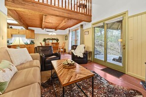 A cozy living room with a wooden ceiling, a dining area, and a view through a glass door. - Wren Cottage; private & peaceful. Gatlinburg, Pigeon Forge (Sevierville)