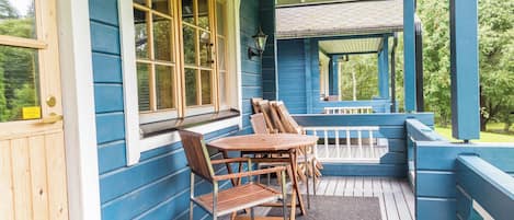 A covered porch with wooden furniture and a brick wall.