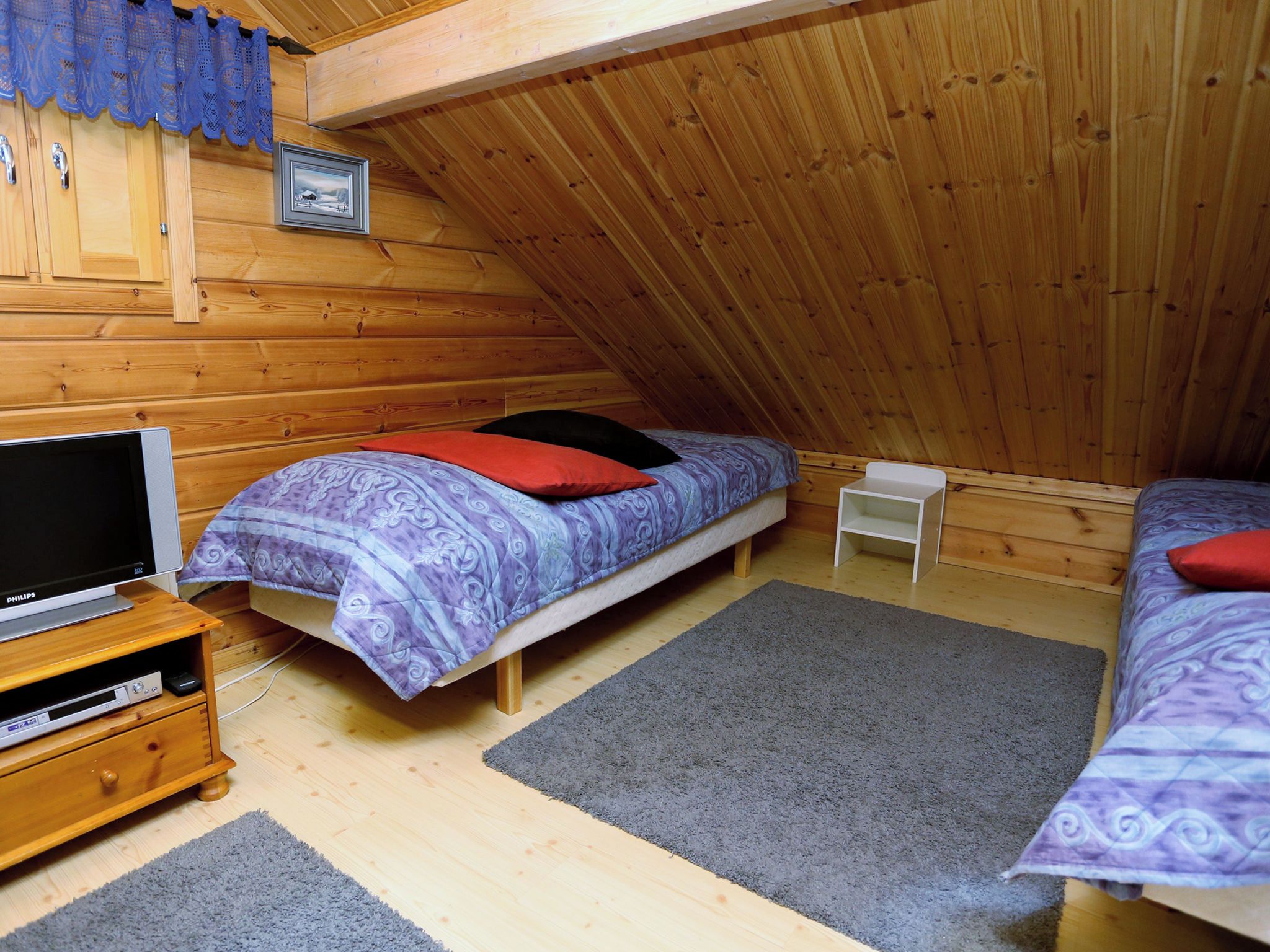 Une chambre confortable située sous les toits, avec un plafond en pente, des murs en bois, un lit avec une literie à motifs, une petite table de chevet et un téléviseur posé sur un meuble en bois.