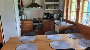 Une cuisine compacte équipée d’une cuisinière, d’un four à micro-ondes et d’un évier. On y trouve quatre chaises disposées autour d’une table en bois, sur laquelle sont posés des sets de table.
