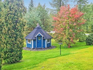 A small blue gazebo with a peaked roof surrounded by lush greenery and trees.