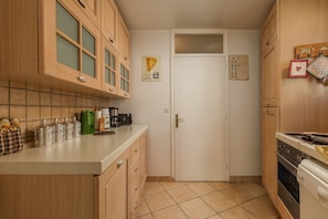 Cozinha compacta com armários de madeira, painel de azulejos, cafeteira e fogão.