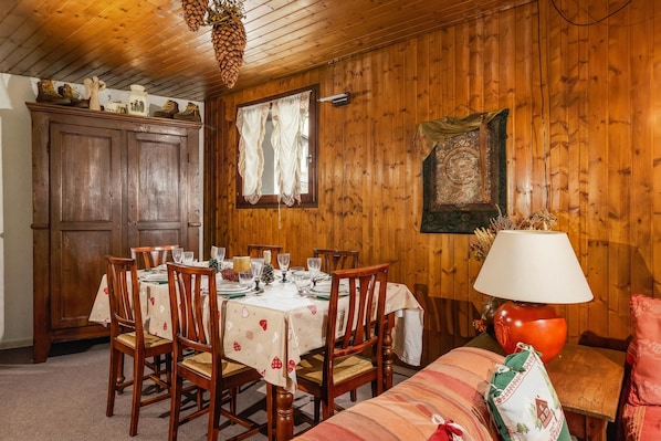 Uma sala de jantar com mesa de madeira posta para quatro pessoas, rodeada por cadeiras de madeira.