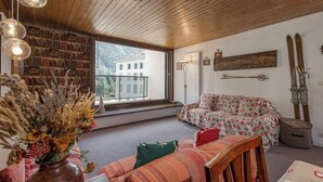 Une pièce avec un plafond en bois, un canapé, une table en bois, un vase contenant des fleurs séch ées et une fenêtre donnant sur un immeuble.