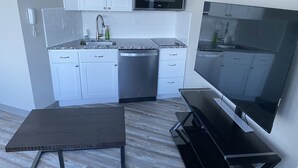 Una cocina moderna con armarios blancos, lavavajillas de acero inoxidable, microondas integrado y un televisor de pantalla plana grande.