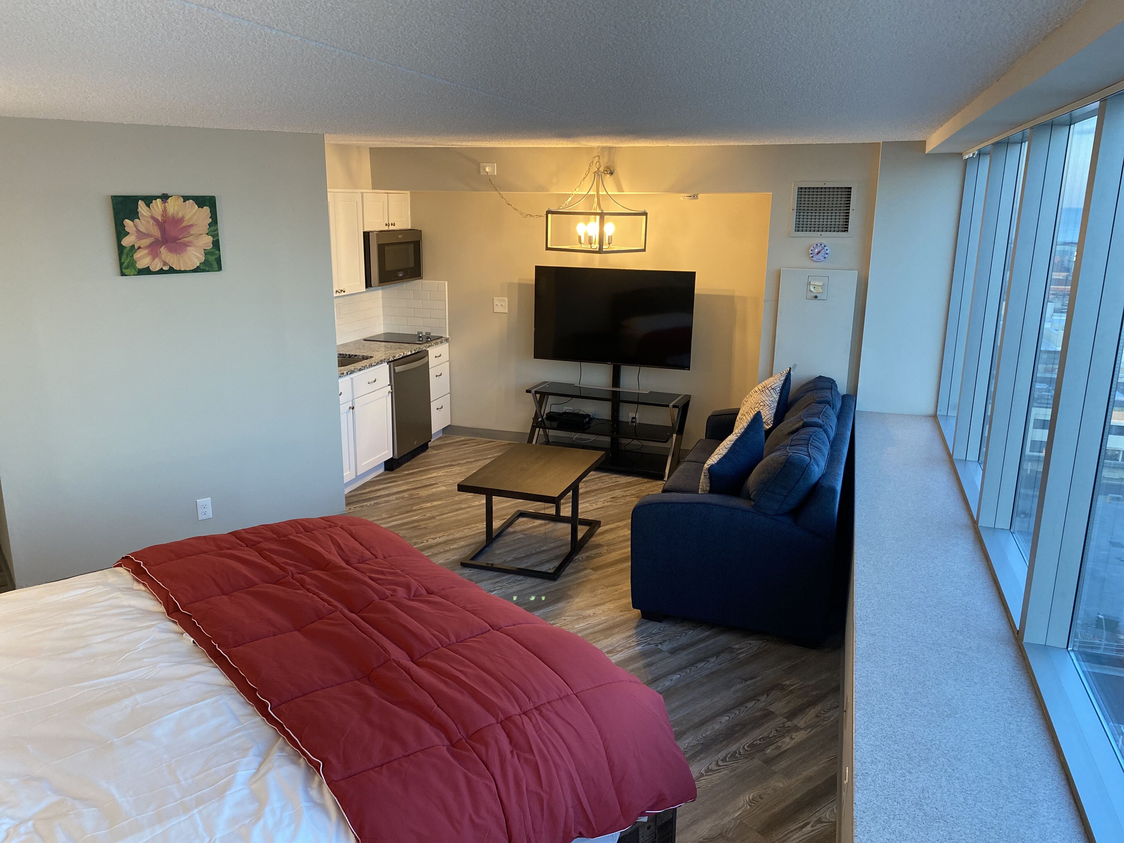 A compact living space with a bed, a sofa, a TV, a kitchenette, and a dining area.