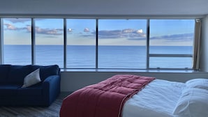Habitación de hotel con un amplio ventanal que ofrece vistas al mar y a la costa distante.