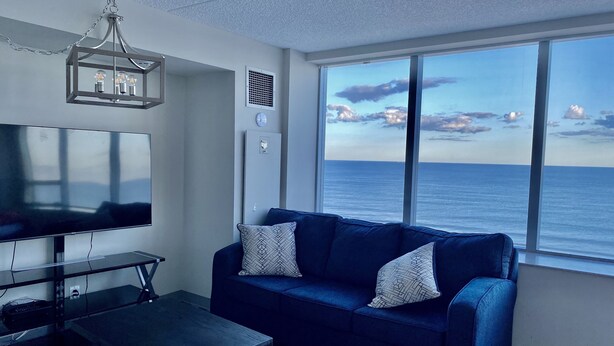 Una sala de estar moderna con un televisor grande, un sofá azul y vistas al océano.