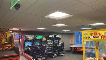 Una habitación con juegos de arcade, una máquina de garras con taxis de juguete y un aro de baloncesto.