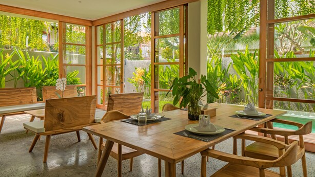 A spacious dining area with wooden furniture and large windows offering a view of lush greenery. - Villa Avyathi at Anandathu Villas - Tropical 2BR Contemporary Villa in Canggu (Bali)