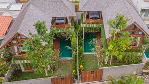 A modern house with a sloped roof, multiple windows, and a small garden area with various plants and flowers. - Villa Avyathi at Anandathu Villas - Tropical 2BR Contemporary Villa in Canggu (Bali)