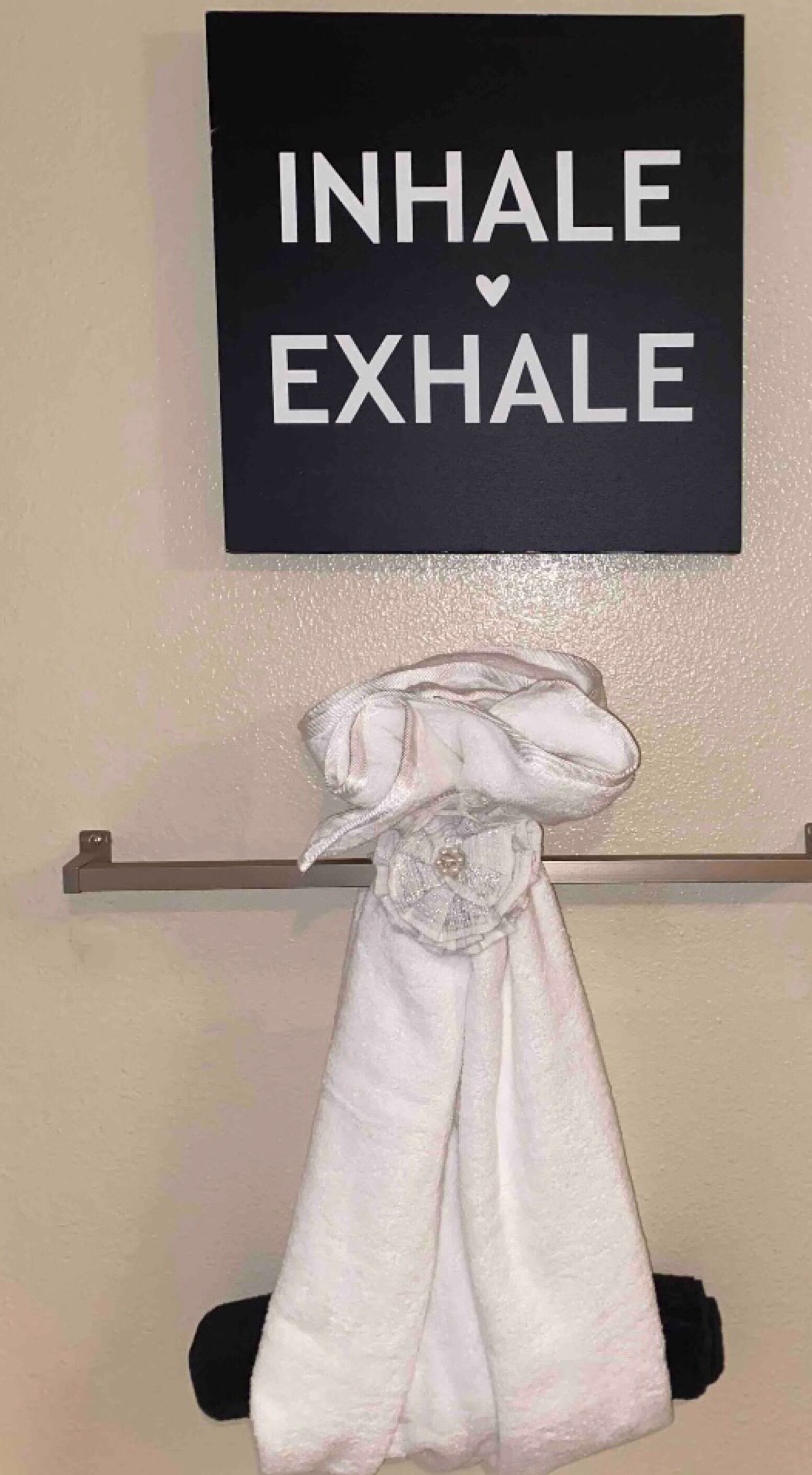 A towel rack with a folded towel and a sign above it that reads "INHALE EXHALE".
