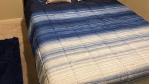 Un lit avec une tête de lit sombre et une couvre-lit à rayures bleues et blanches.