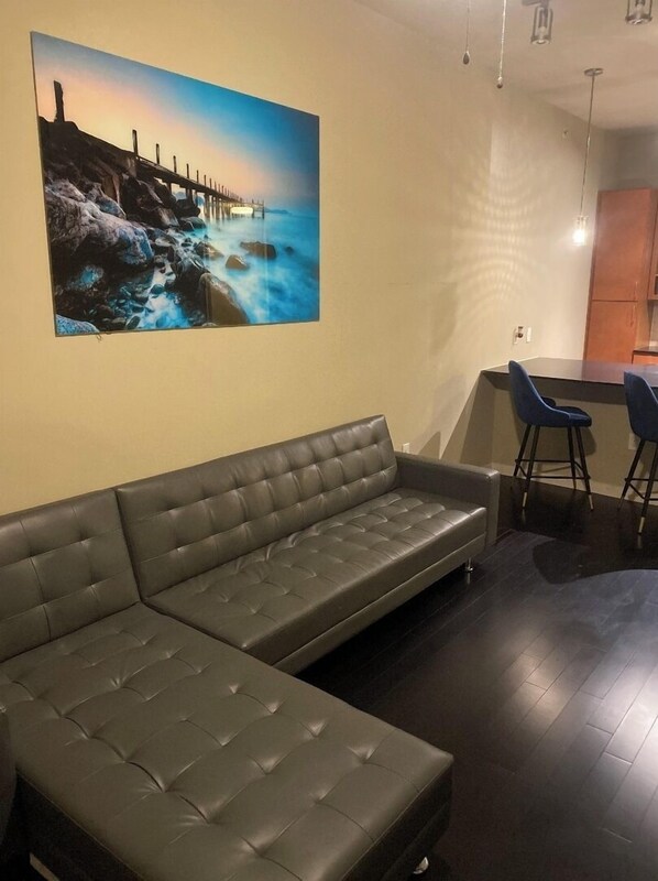 Un salon moderne avec un canapé en cuir foncé, un tableau représentant un paysage côtier et un coin bar avec des tabourets.