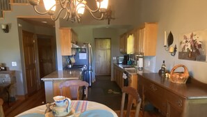 A dining area with a chandelier, wooden dining table, chairs, and a kitchen in the background. - Sky Dog Pet Friendly Home Dupont Brevard Hiking Mountain Biking Porch Waterfalls (Brevard)
