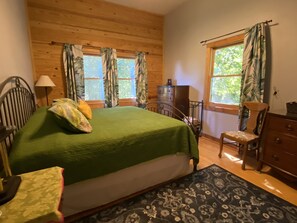Een slaapkamer met een groot bed, houten wanden, een dressoir, een stoel en een raam met gordijnen.