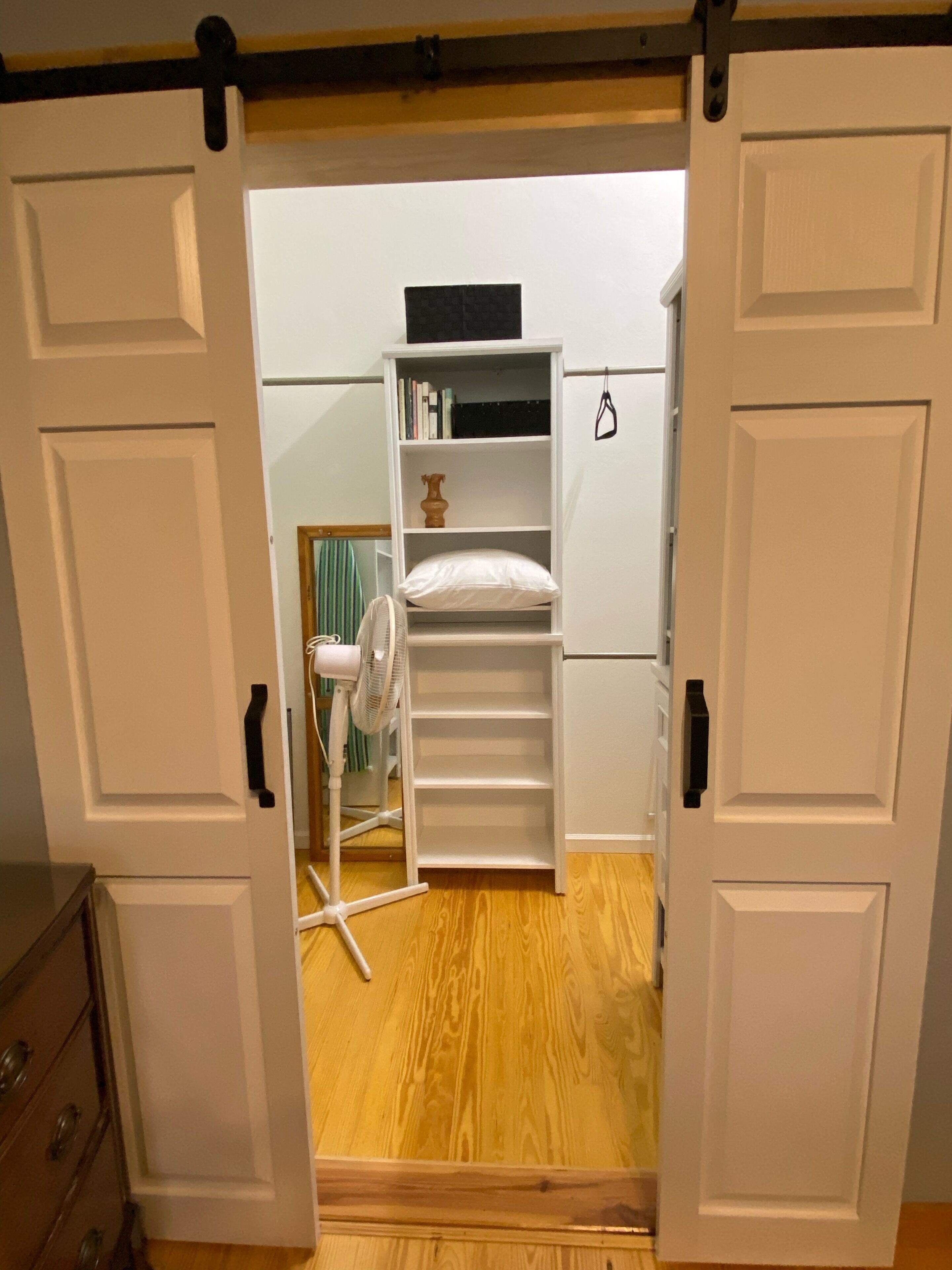 Una habitación con un armario blanco, un ventilador blanco y suelo de madera.