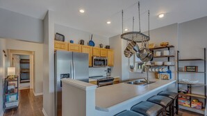Una cocina moderna con una isla central, electrodomésticos de acero inoxidable, armarios de madera y una barra para colgar ollas.