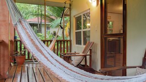Eine Hängematte auf einer Holzterrasse mit Blick auf ein Haus und Grünflächen.