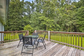 A wooden deck with a table and chairs, surrounded by a wooden railing, overlooking a lush green lawn and dense forest. - Quiet Home w/ Fire Pit - 1 Mi to Downtown Acworth! (Acworth)