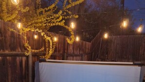Un bain à remous avec un éclairage bleu, entouré d’une clôture en bois et illuminé de guirlandes lumineuses.
