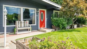 Une maison avec une porte rouge, une clôture blanche en bois et un banc à l’extérieur.