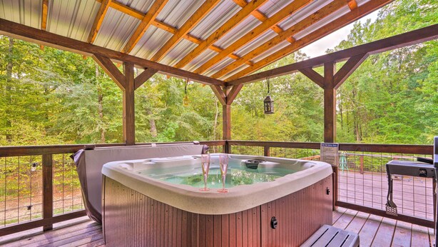 A hot tub with two champagne glasses, a wooden deck, and a metal roof. - Pet-Friendly Home w/ Deck in Broken Bow! (Broken Bow)