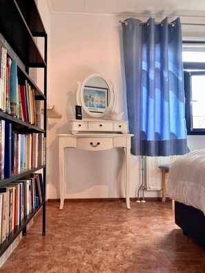 A bedroom with a white dresser, a bookshelf, a bed, and a window with a curtain.