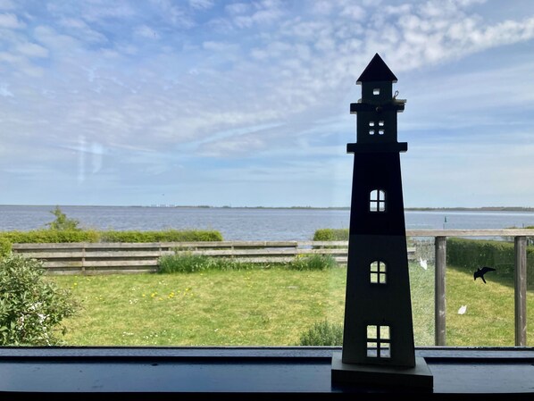 A model tower with windows, a grassy area, a wooden fence, and a body of water in the background.