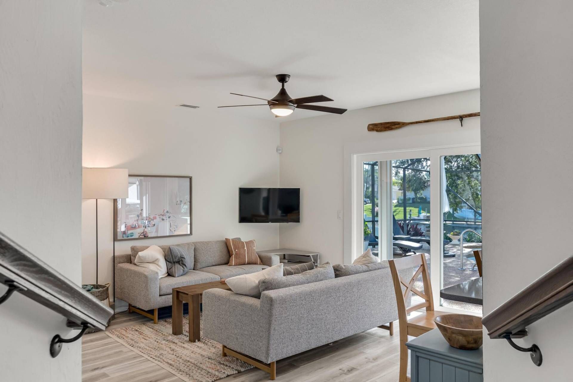 A modern living room with a grey sectional sofa, a flat-screen TV, and a ceiling fan.