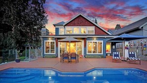 A two-story house with a swimming pool, outdoor seating, and a large window overlooking the pool.