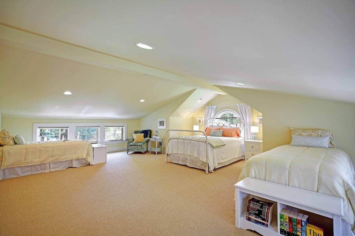 A spacious attic bedroom with two beds, a reading nook, and a window providing natural light.