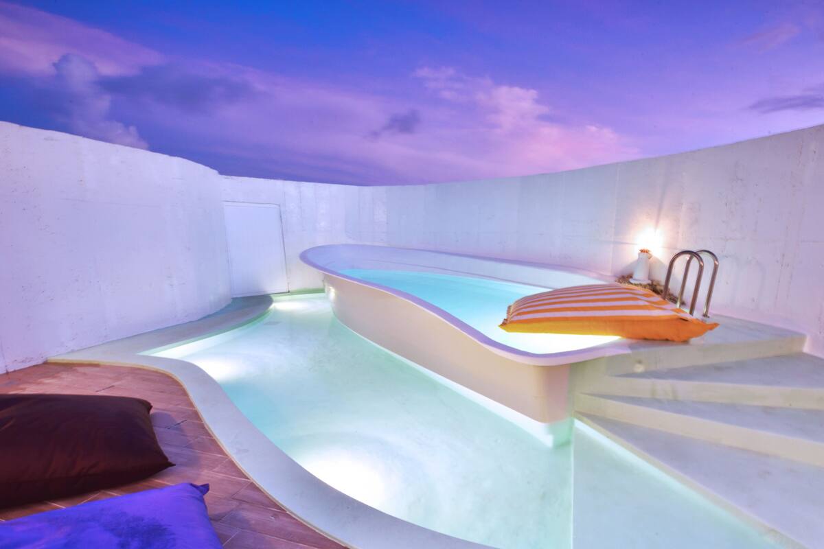 Una piscina interna moderna con un design curvo, un piccolo angolo relax con un cuscino e una scala che conduce a un livello superiore.