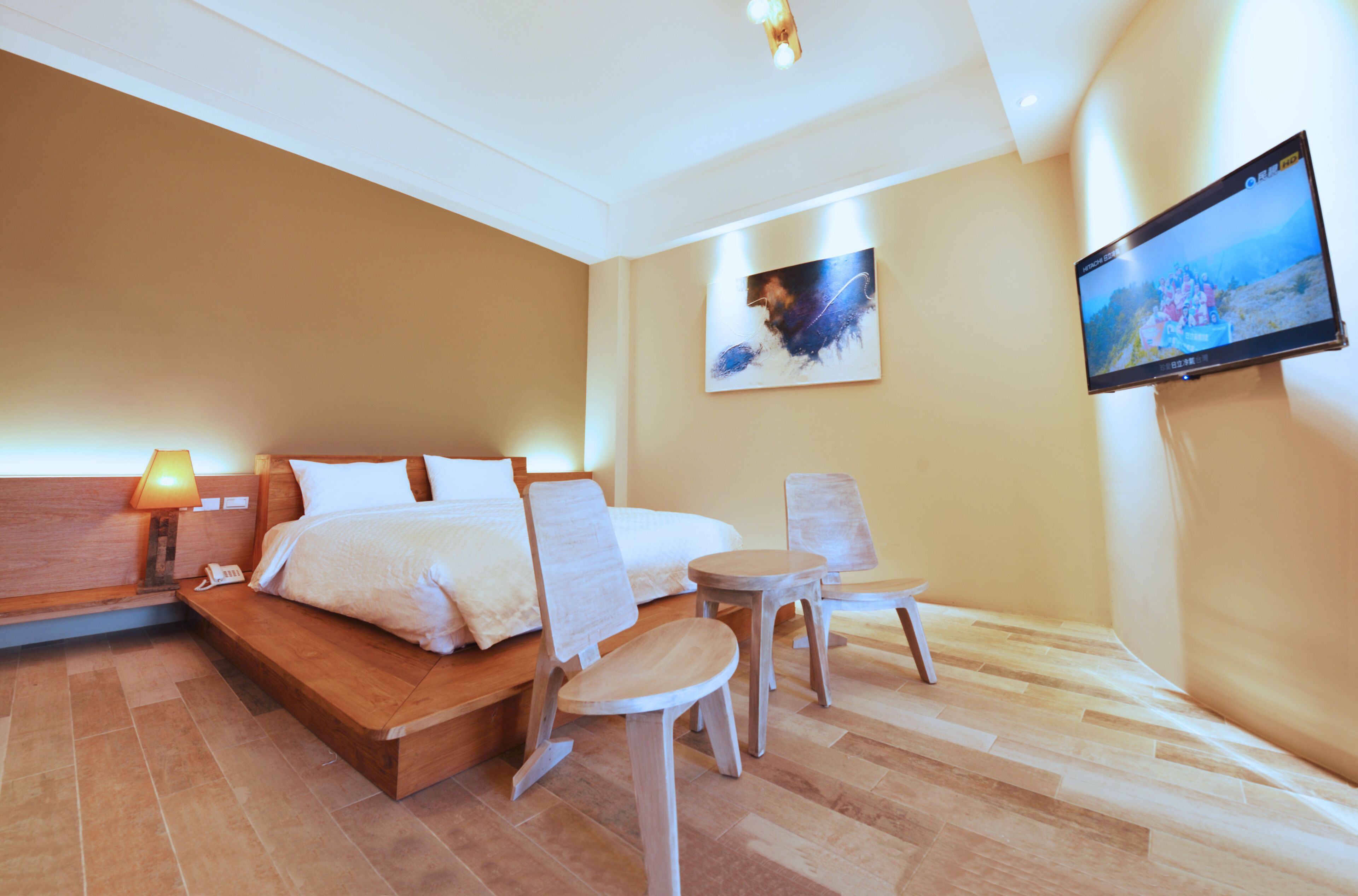 Een hotelkamer met een bed, nachtkastje, lamp, stoelen en een televisie aan de muur.