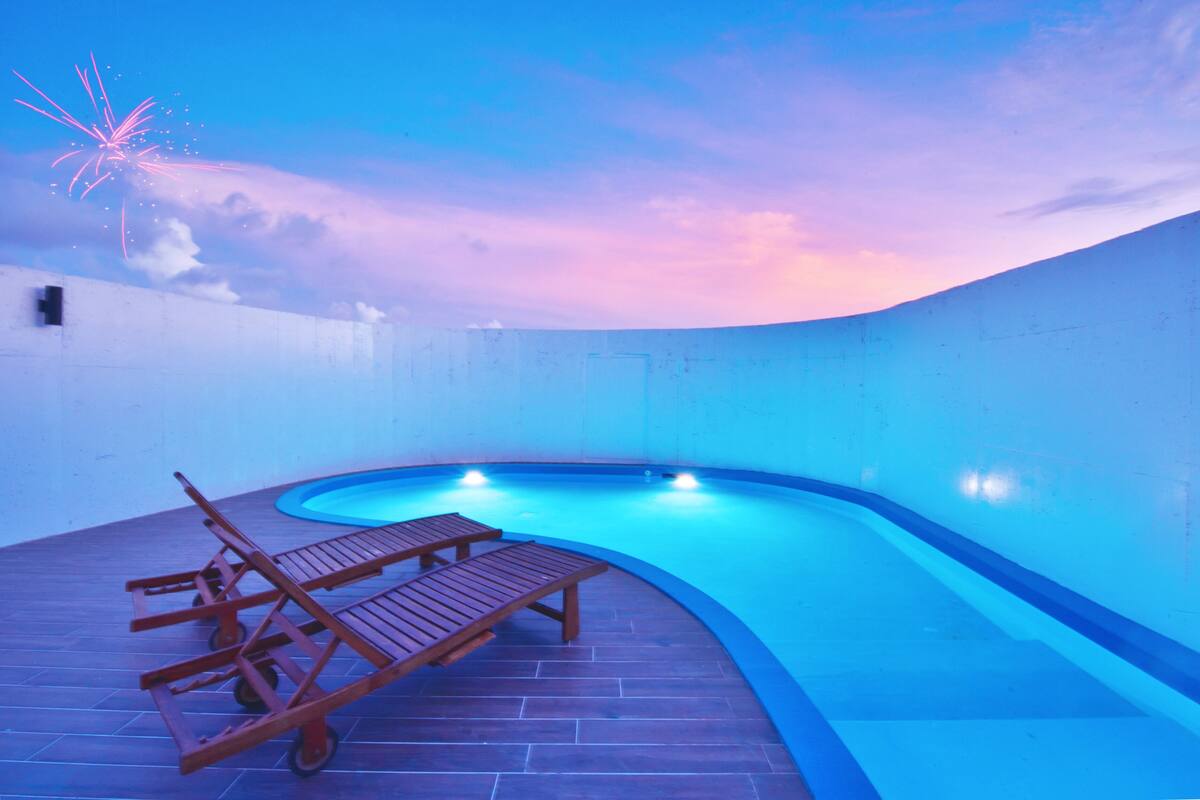 Una piscina a forma di curva con sdraio in legno e un solarium piastrellato.