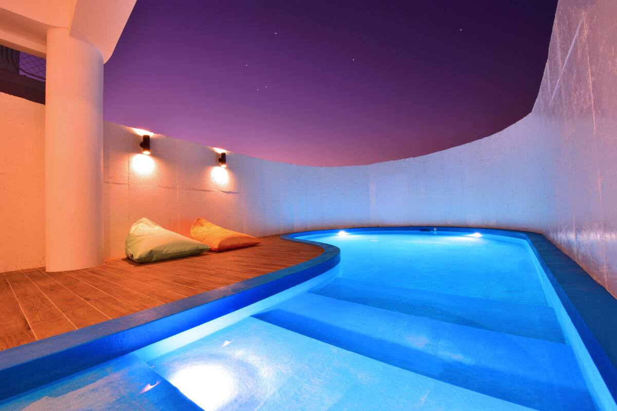 Una piscina interna moderna con un pontile in legno e due luci a parete.