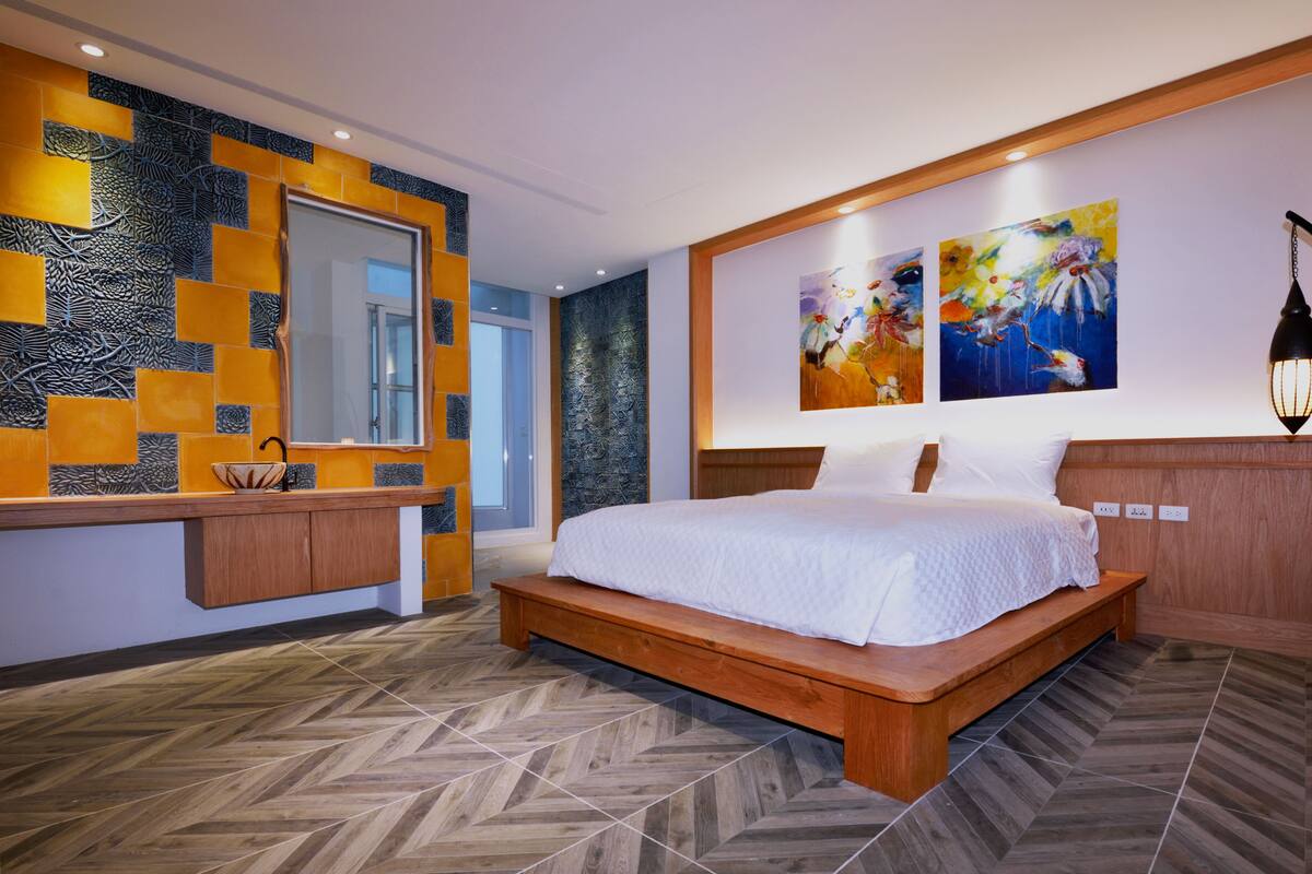 Camera da letto moderna con un letto grande, una testiera in legno, una panca integrata, uno specchio e due quadri appesi al muro.