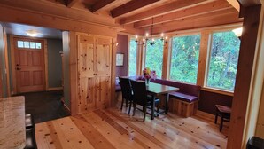 A wooden interior with a dining area, large windows, and a door.