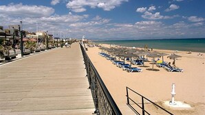 Une promenade en bois menant à une plage où se trouvent des chaises longues et des parasols.
