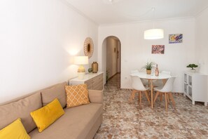 A living area with a sofa, a dining table with chairs, a lamp, and a small cabinet.