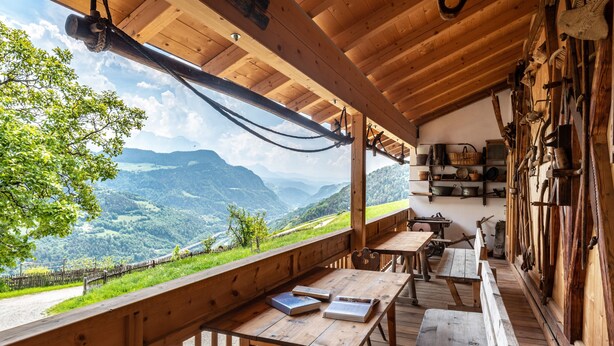 A wooden deck with a view of a mountainous landscape, wooden tables, benches, and rustic kitchen utensils. - Holiday Apartment "Dolomiten Winklerhof" with Mountain View, Garden & Wi-Fi (Villanders)