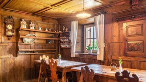 A wooden interior with a dining table, chairs, shelves with dishes, a clock, and a window with curtains. - Holiday Apartment "Dolomiten Winklerhof" with Mountain View, Garden & Wi-Fi (Villanders)