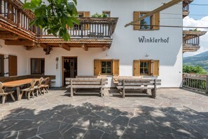 A building named 'Winklerhof' with a stone patio, wooden benches, and a balcony.