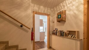 A staircase with a fire extinguisher, a wooden door leading to a room, and a shelf with books and a first aid kit.