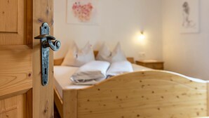 A wooden door with a metal handle, a bed with white bedding, a bedside table, and a wall with a heart-shaped decoration.