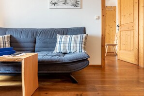 Un salon moderne avec un canapé gris, des coussins à carreaux, une table basse en bois et une porte en bois à l’arrière-plan.